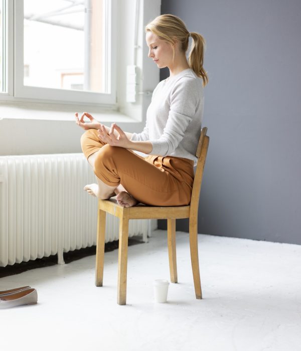 Young woman sitting on chair in office practicing yoga